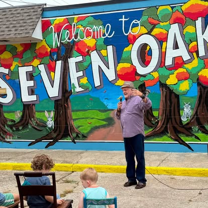 A speaker in front of the Welcome to Seven Oaks mural