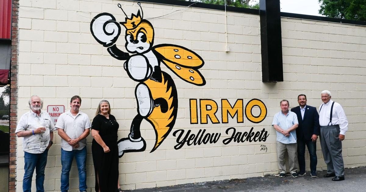 The Irmo Yellow Jackets mural, a cartoon yellow jacket boxer painted on a cinder-block wall, with six supporters standing beside it