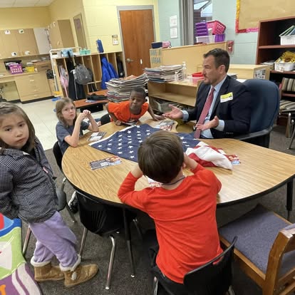 Gabriel Penfield showing students an American flag at a classroom table
