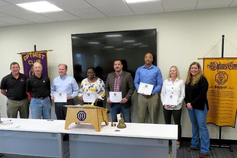Optimist Club members holding certificates at a Friday meeting, with the club banner and the Optimist Creed