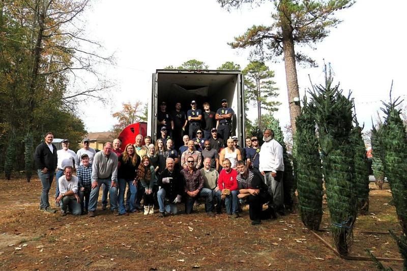 Optimist Club volunteers and firefighters gathered in front of a truck of Christmas trees at the club&rsquo;s tree lot
