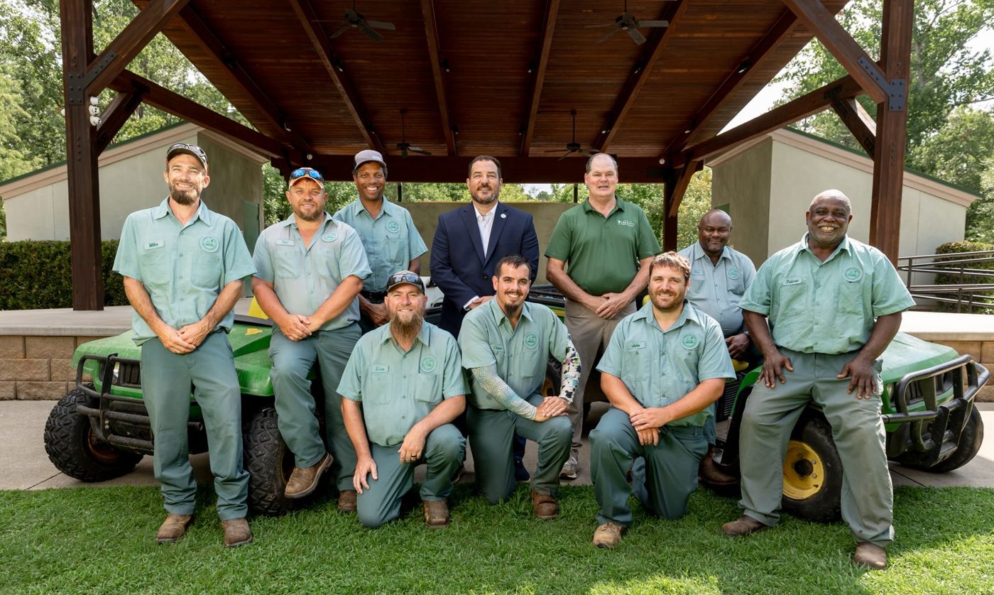 Gabriel Penfield with the Town of Irmo Public Services crew in green uniforms, in front of a park pavilion with two utility vehicles